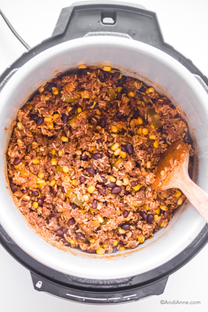 Looking down in an instant pot at the burrito bowl mixture with a wood spatula.