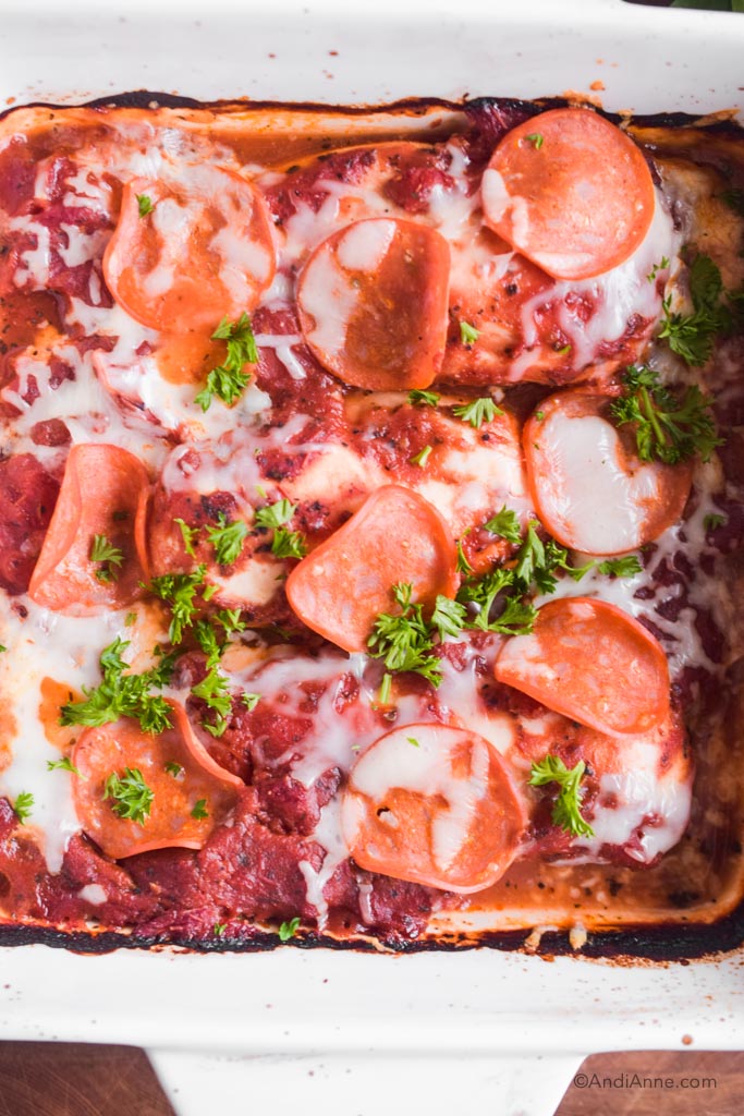 close detail of low carb pizza chicken in white dish topped with chopped parsley, pepperoni slices and mozzarella cheese.