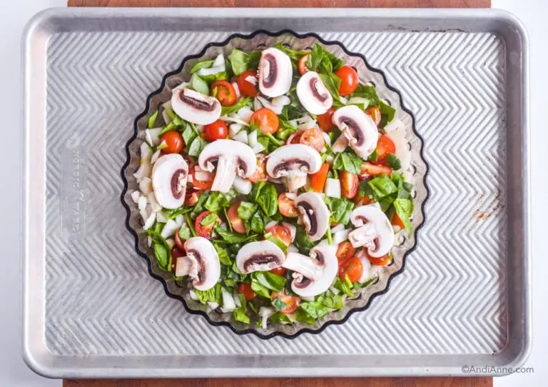 Raw sliced mushrooms, tomatoes and spinach in a baking dish.