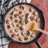 A frying pan with brown sauce and meatballs and a wood spatula.