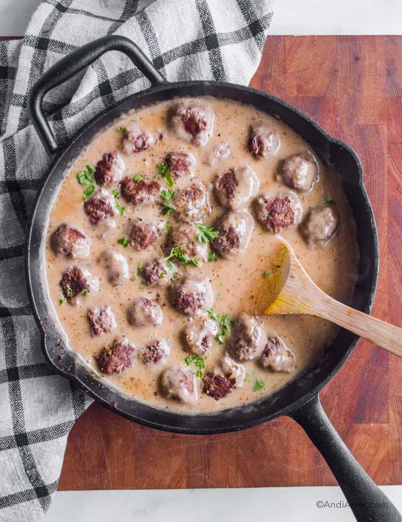 swedish meatballs in a black cast iron skillet on wood cutting block with dish towel.