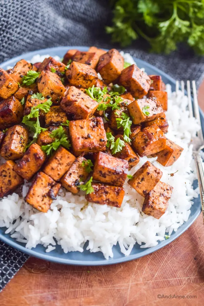 Close up of cooked tofu on a bed of white rice with chopped parsley sprinkled on top.