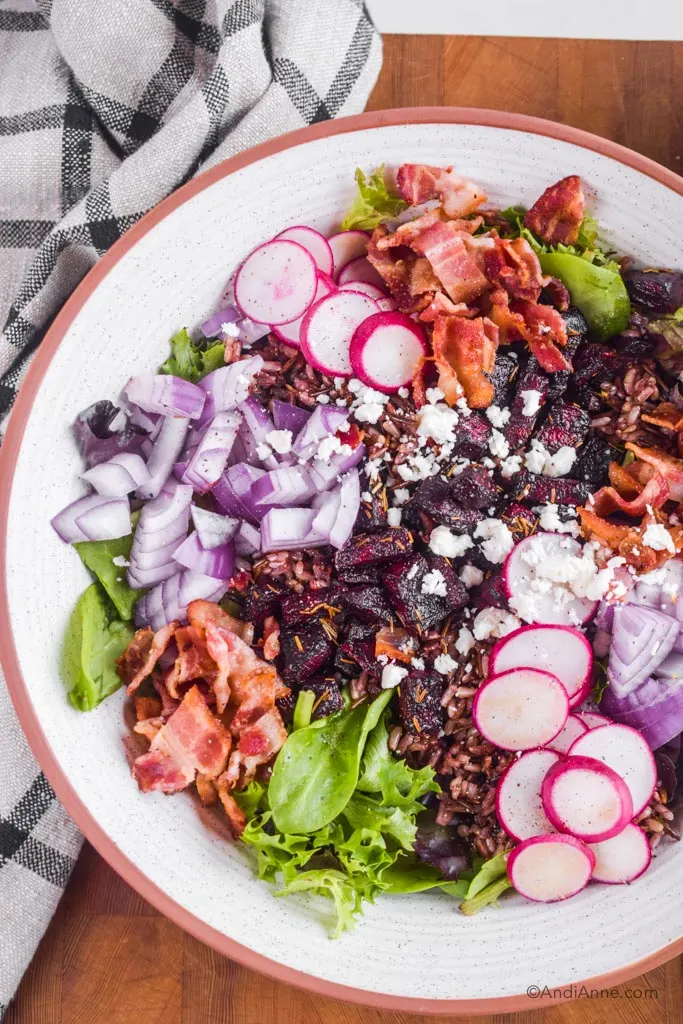 beet bacon feta salad in a white bowl with kitchen towel beside it.