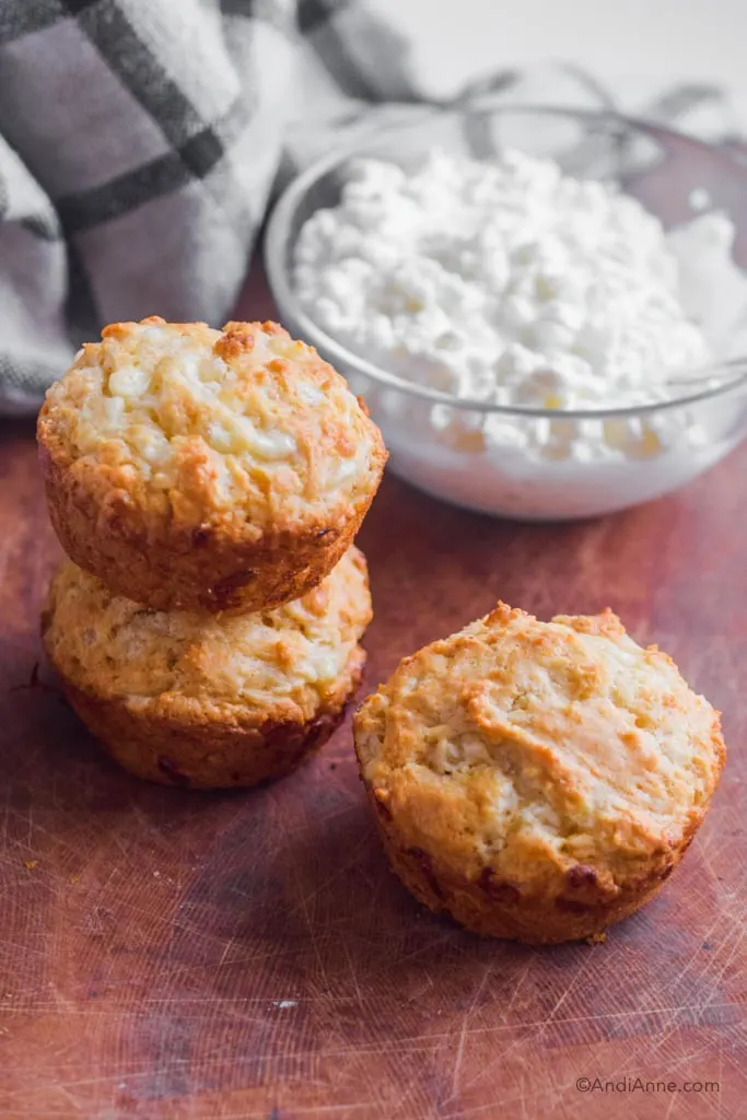 three cottage cheese muffins with a bowl of cottage cheese behind them