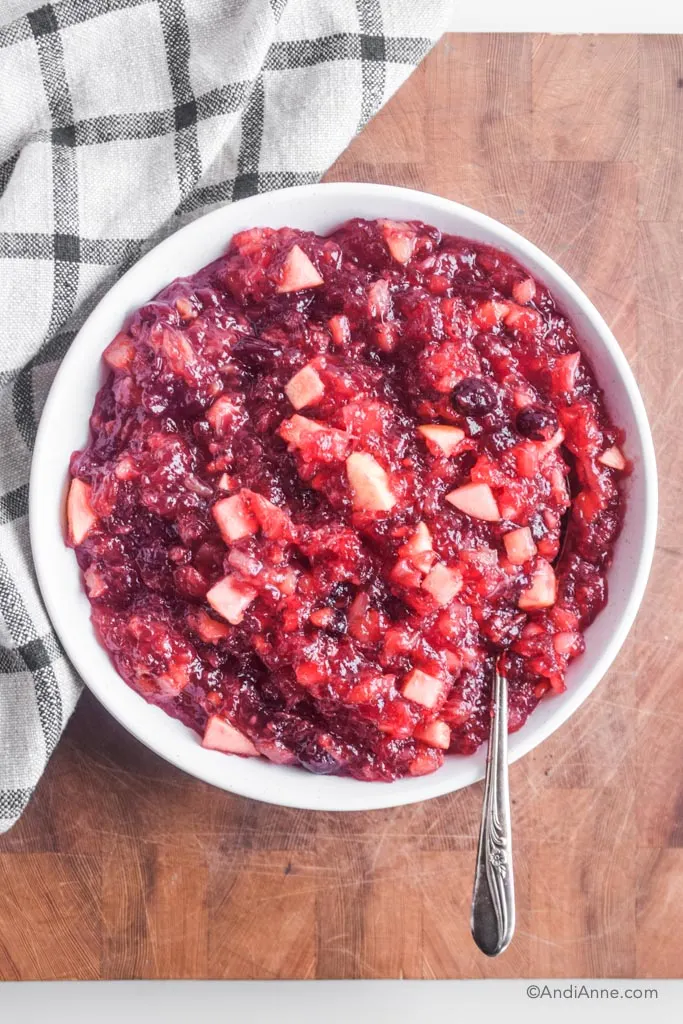 cranberry pineapple jello salad in a white dish with spoon. It sits on a butcher block with a kitchen towel beside.