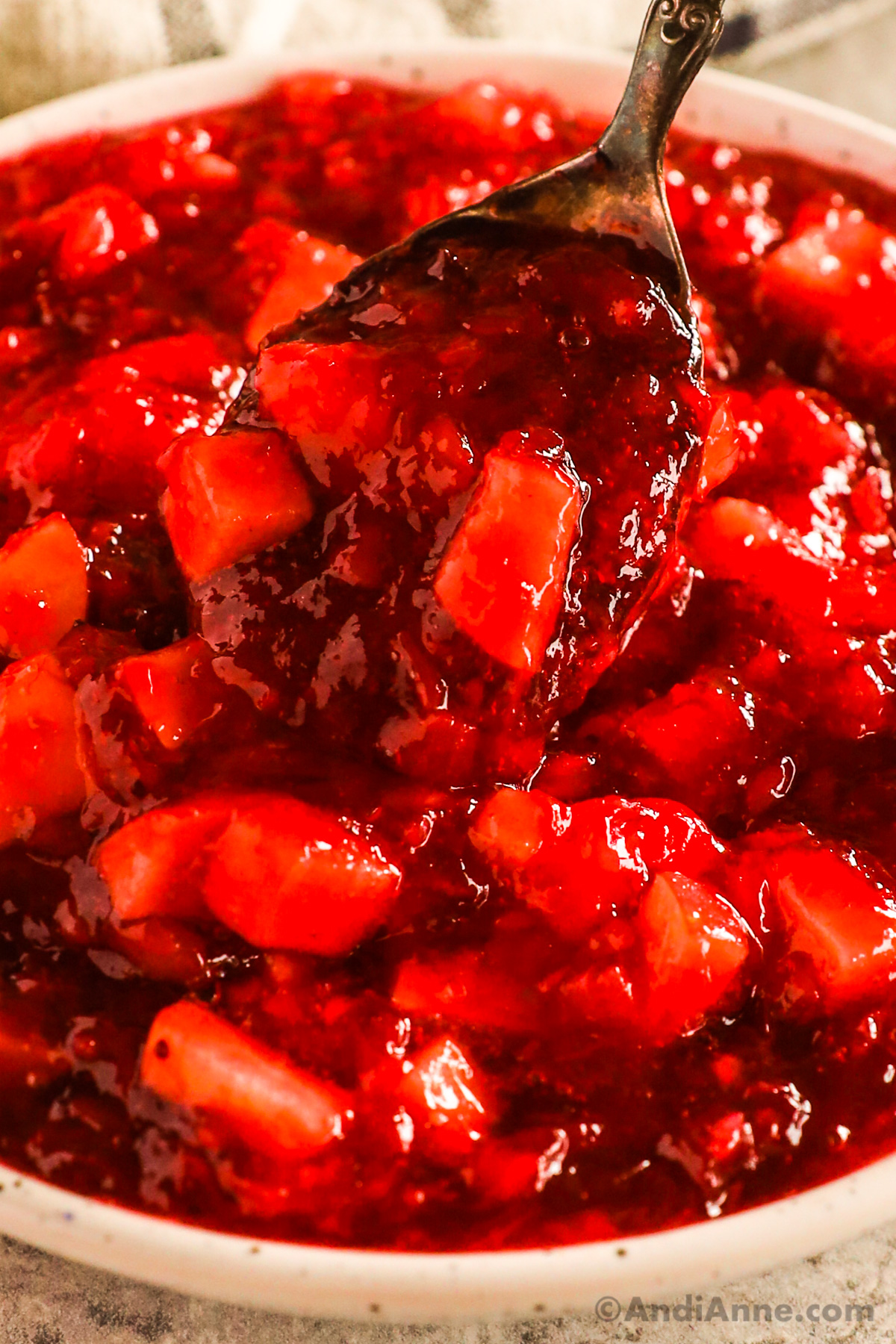 A spoon scooping cranberry jello salad with pices of apple.