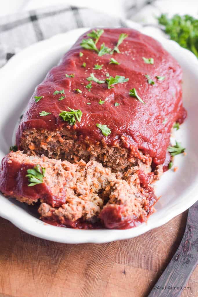 keto vegetable meatloaf with sprinkled parsley on top sitting in a white dish with a kitchen towel blurred in background.