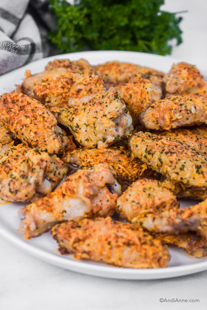baked parmesan chicken wings on a white plate with parsley and kitchen towel in background