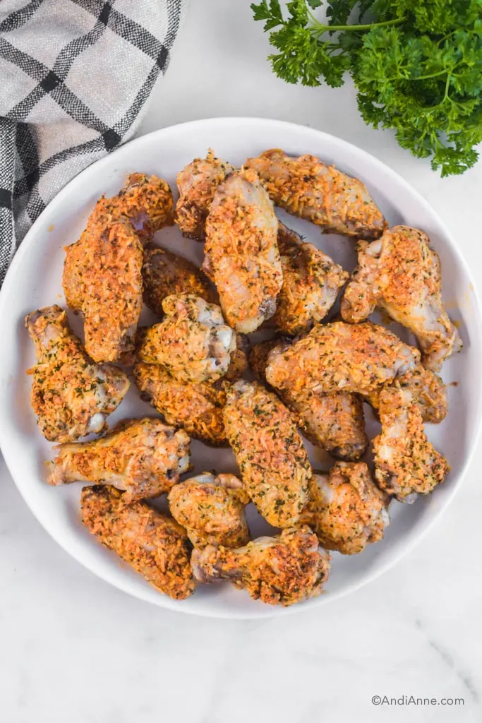 chicken wings on a white plate with parsley and kitchen towel surrounding it.