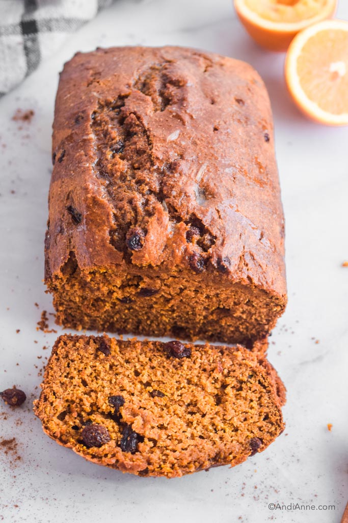 pumpkin raisin loaf sliced into with orange and kitchen towel behind it