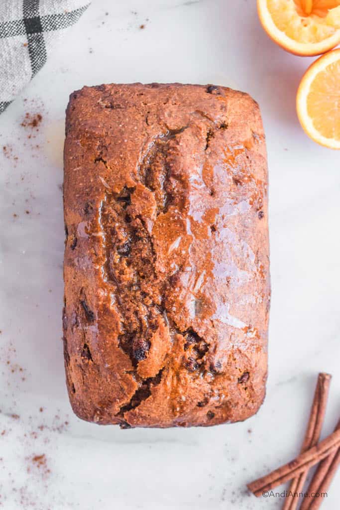 pumpkin raisin loaf with orange glaze on a marble counter with sliced orange and cinnamon sticks around it