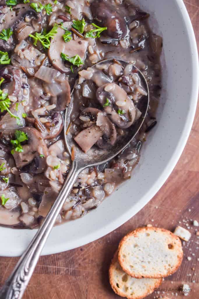 Close up of wild rice mushroom soup with a silver spoon. Chopped parsley and croutons beside the bowl.