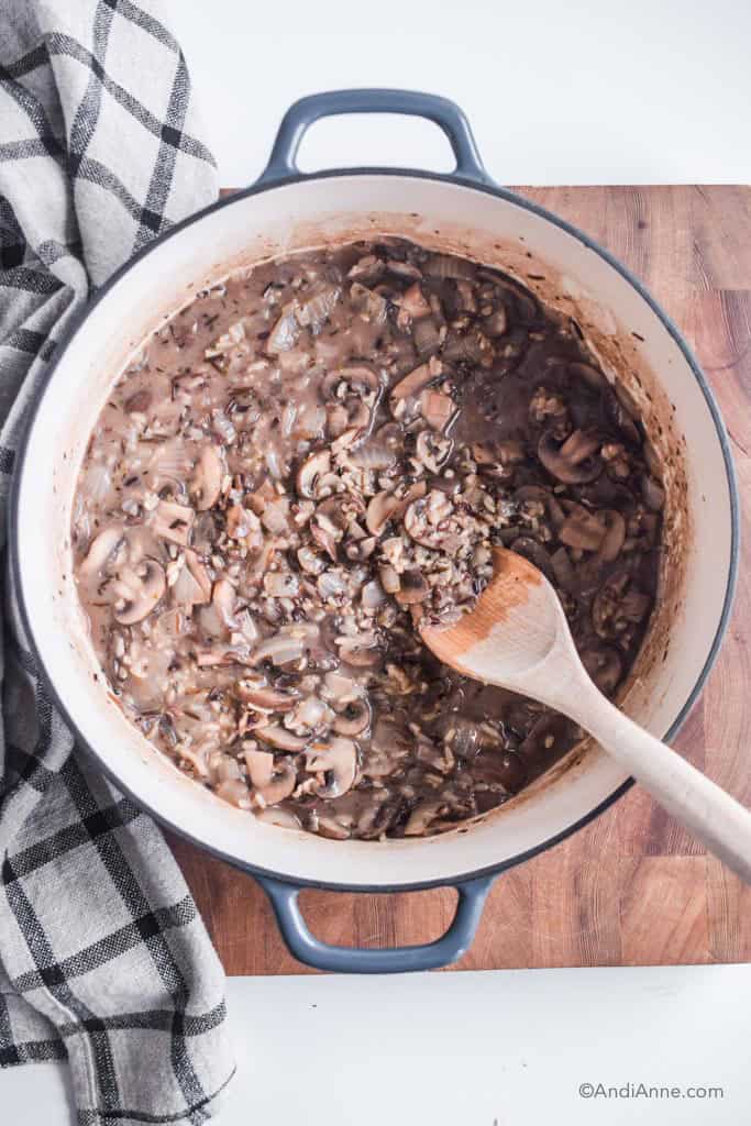 Cast iron dutch oven with wild rice mushroom soup inside and wooden spoon.