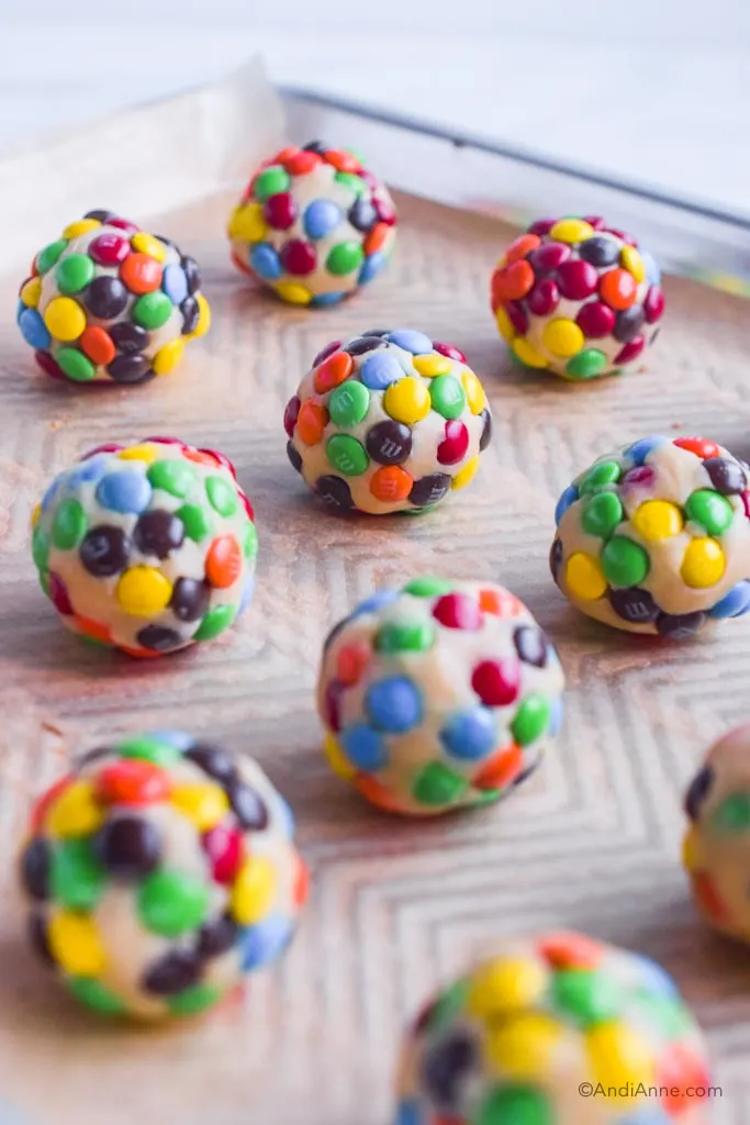Balls of cookie dough rolled in mini M&Ms on a baking sheet.