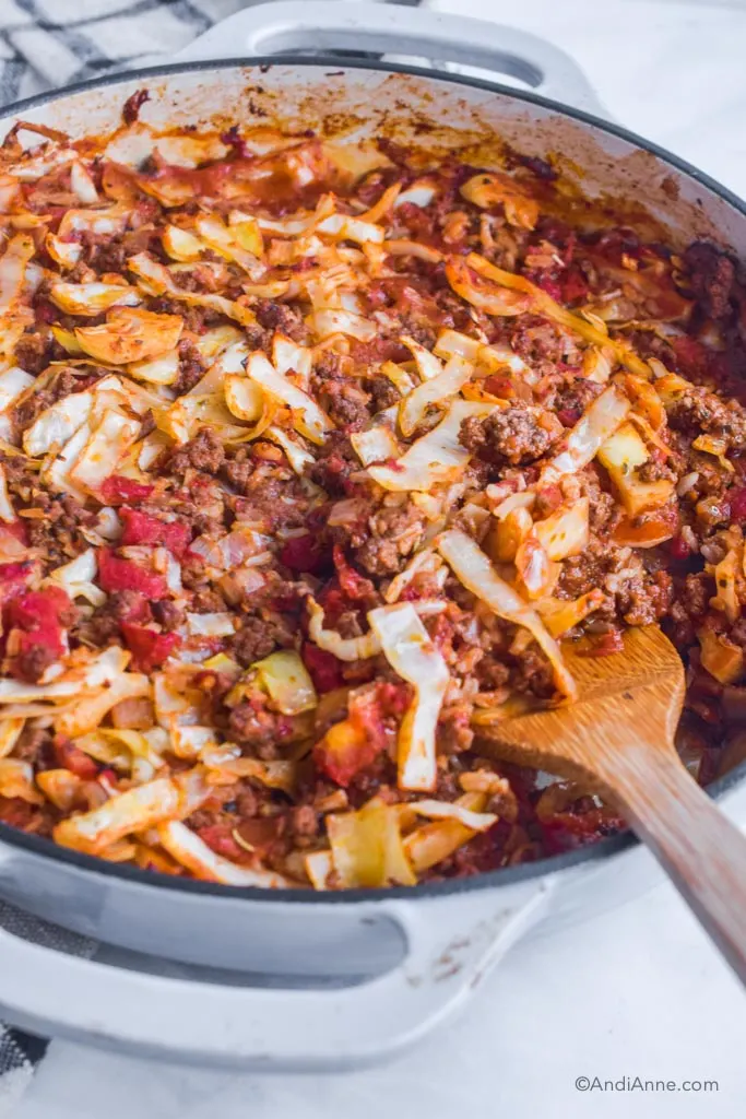 Beef and cabbage roll recipe in a white and grey pot with a wood spoon beside. 