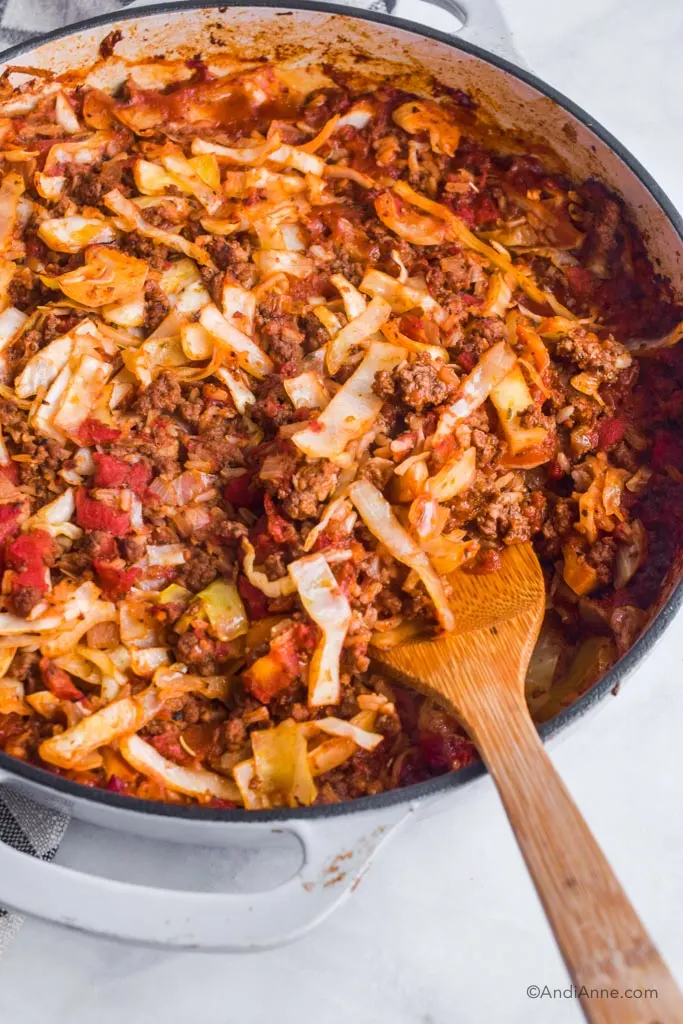 Side angle of beef rice cabbage casserole in grey pan with wood spoon