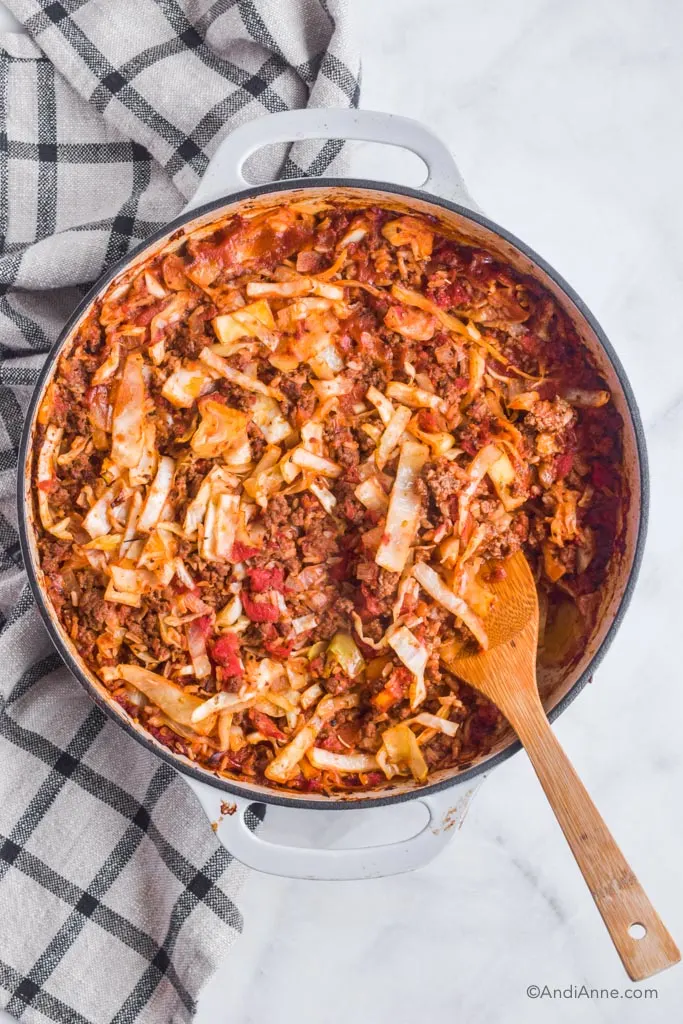 beef rice cabbage casserole in Lodge gray cast iron braiser with wood spatula and kitchen towel beside it.