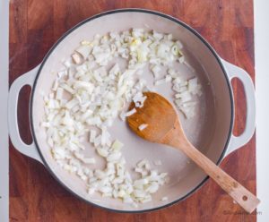 chopped onion in a white pan with wood spatula