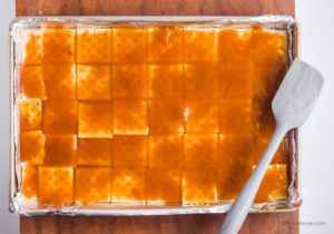 caramel sauce poured overtop of saltine crackers in baking sheet with grey spatula beside it