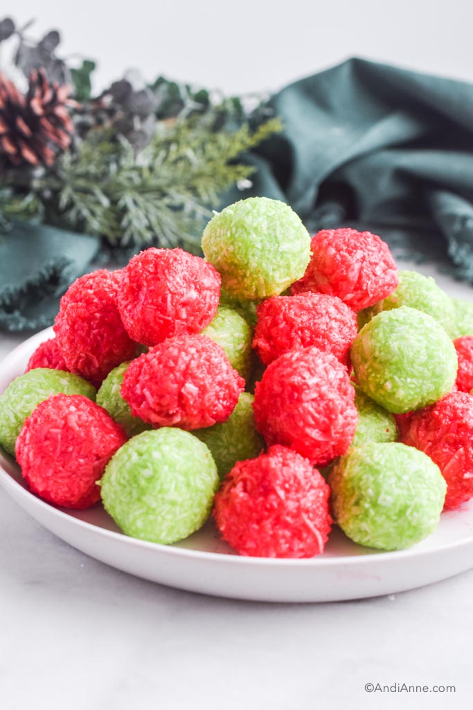 Pile of green and red christmas jello balls on a white plate with green napkins in the background.