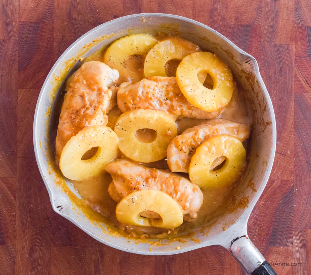 Steel frying pan with chicken breasts, sauce and pineapple slices inside.