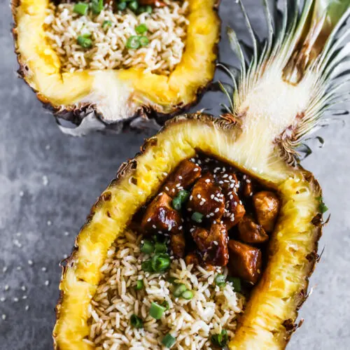 Two pineapple teriyaki chicken with rice in pineapple boats.