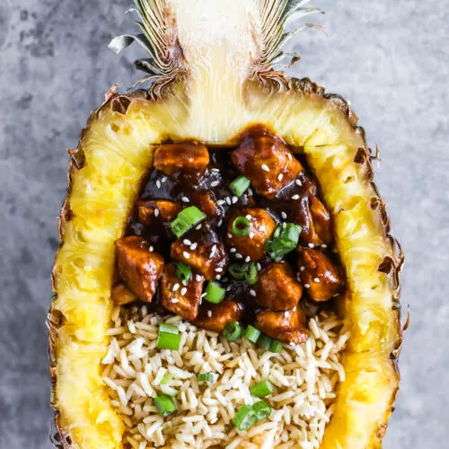 A pineapple boat with cooked rice and teriyaki chicken pieces inside.