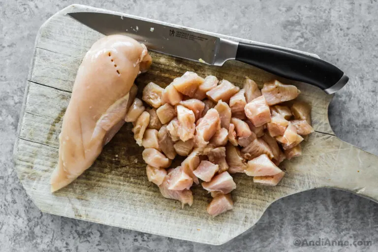 Chopped raw chicken breast with a knife on a cutting board.