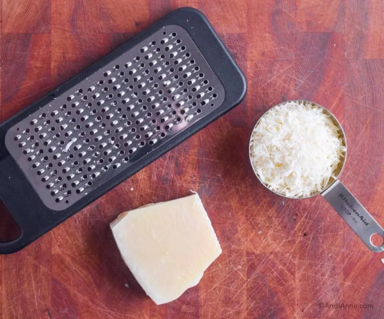 cheese grater, block of parmesan, cup of grated parmesan in measuring cup