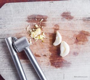 garlic mincer, minced garlic and garlic cloves on cutting board