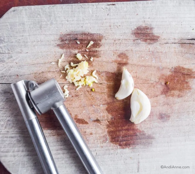 garlic mincer, minced garlic and garlic cloves on cutting board