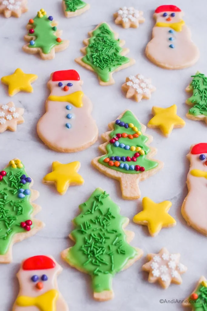 Side angle of decorated christmas sugar cookies on marble counter. Shapes include tree, star, snowmen and snowflake.