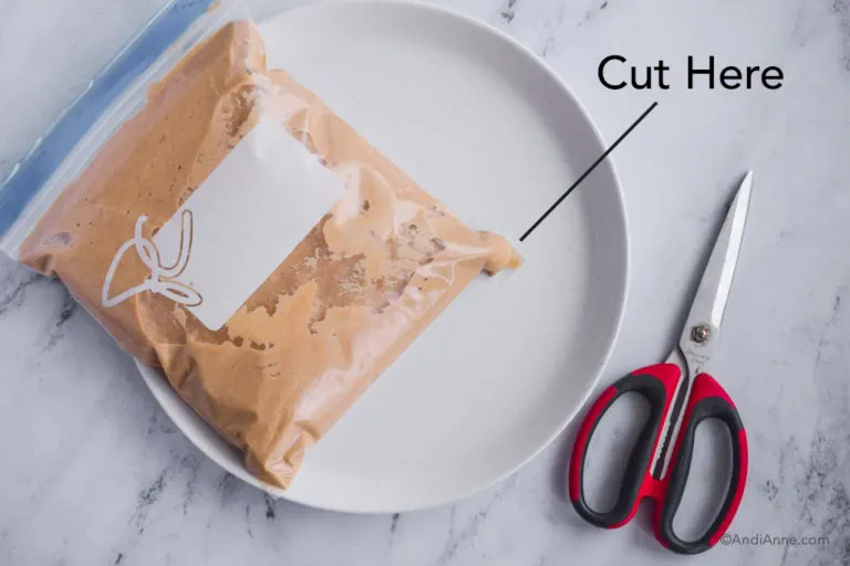 bag of pancake batter with corner snipped. Sitting on white plate with scissors beside it.