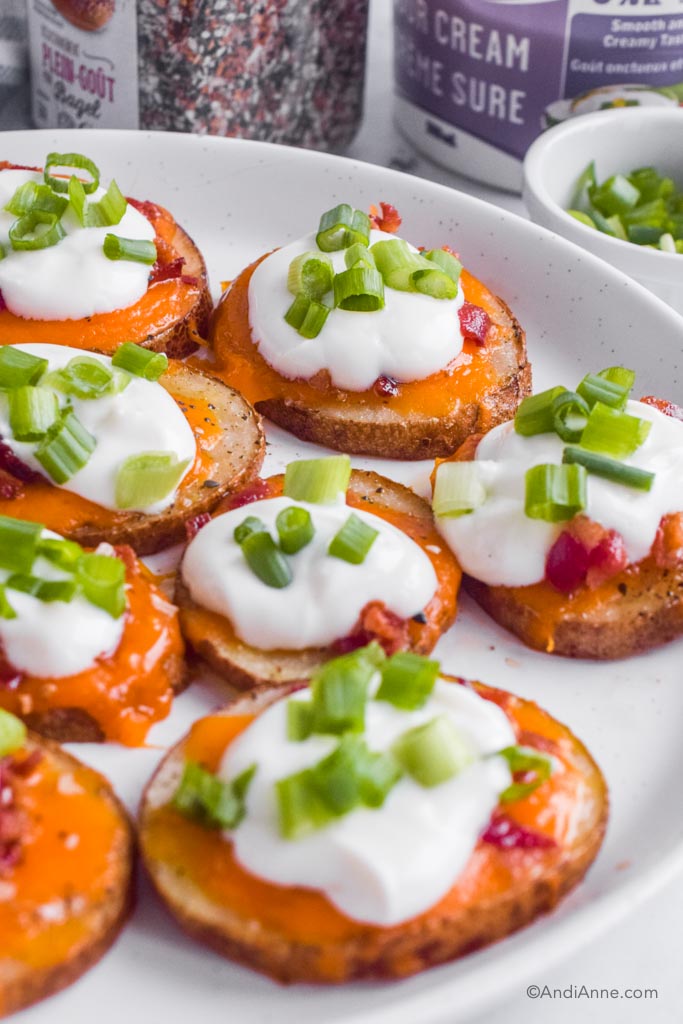 Bacon cheddar potato skins with sour cream and green onions on top. On a white plate.