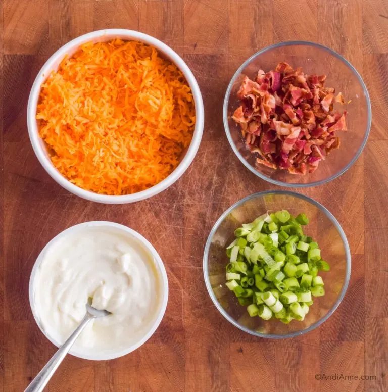 Bowl of cheddar cheese, bowl of sour cream, bowl of crumbled bacon, bowl of chopped green onion.