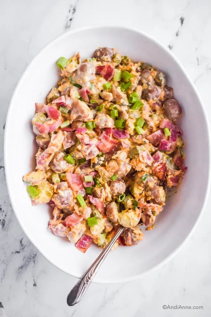 A white bowl with bacon ranch potato salad and a spoon.