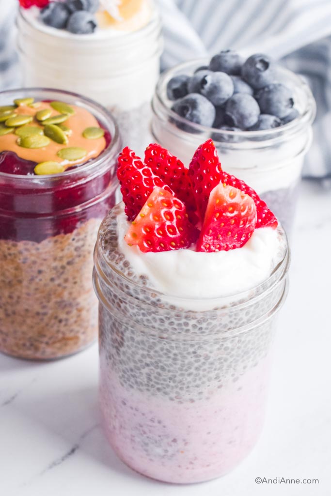 Close up of strawberries and cream chia pudding with sliced strawberries on top and pb & j chia pudding and blueberry flavor in background. 