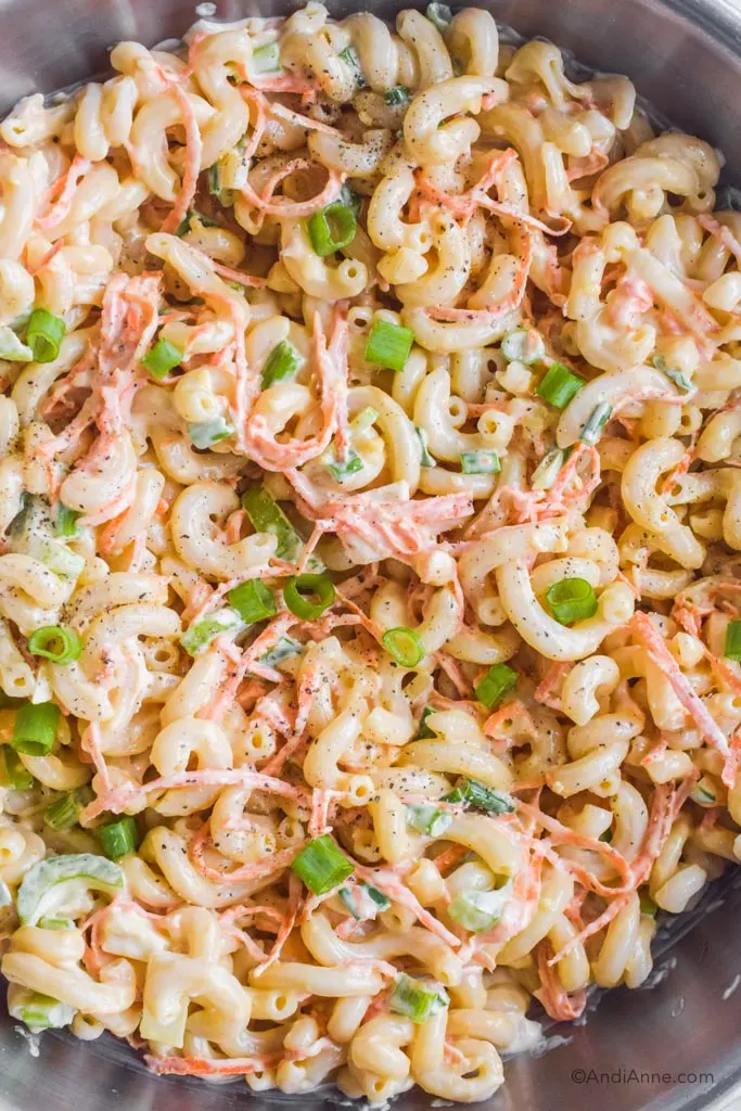 Close up of creamy pasta salad with chopped onion and carrot.