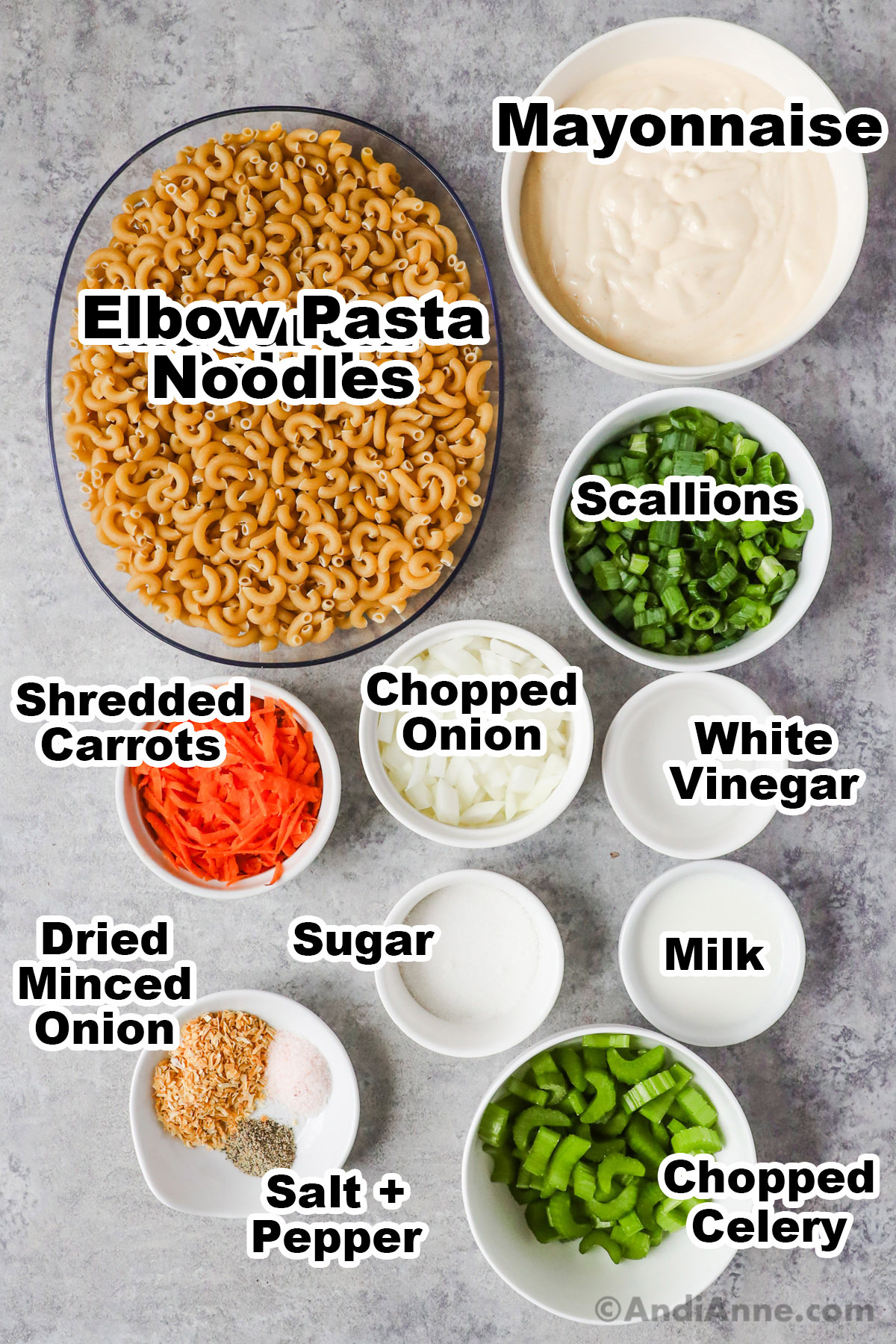 Recipe ingredients in bowls including uncooked pasta noodles, mayonnaise, chopped scallions, shredded carrots, chopped onion, white vinegar, sugar, milk, chopped celery, dried minced onion, salt and pepper.