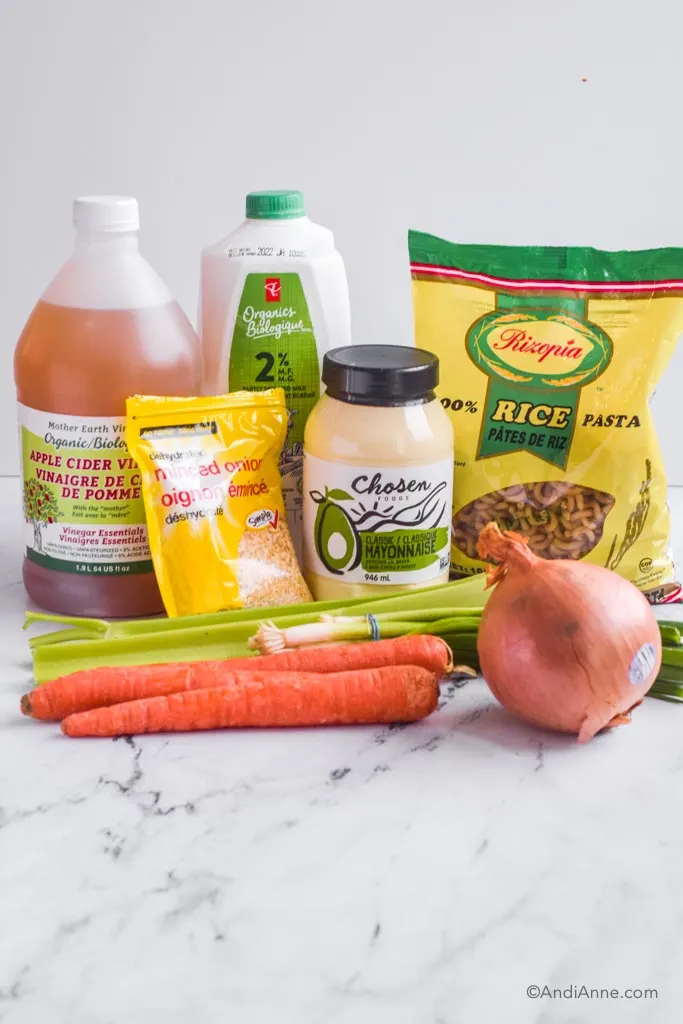 ingredients on counter: jar of apple cider vinegar, milk, mayonnaise, bag of rice pasta, dried minced onion, celery, green onion, yellow onion and 3 carrots