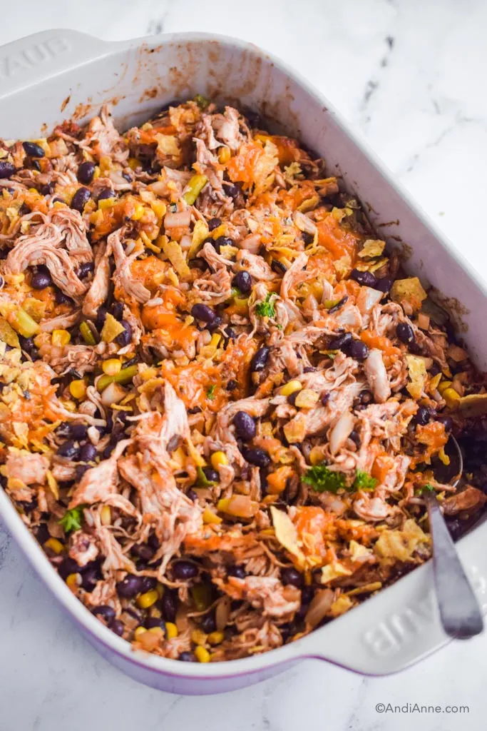 A casserole dish with shredded barbecue chicken, beans, corn and crushed tortilla chips. 