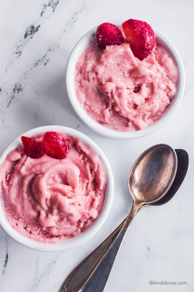 strawberry banana nice cream in two white bowls with silver spoons beside them.