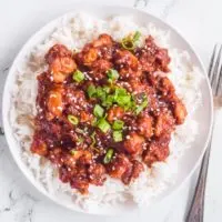 sweet and sour chicken bites over white rice, sprinkled with green onion and sesame seeds. For beside plate.