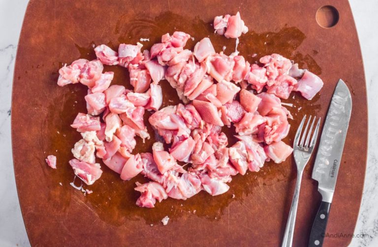 chopped raw chicken on a cutting board with fork and knife