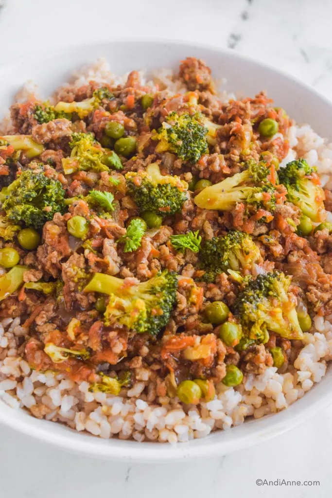 Close up of teriyaki ground turkey rice bowl with broccoli, peas and carrots on a bed of short grain brown rice.