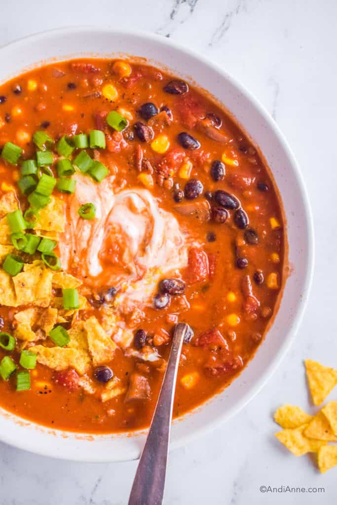 A bowl of black bean tortilla soup topped with sour cream, crushed tortilla chips and chopped green onion. 