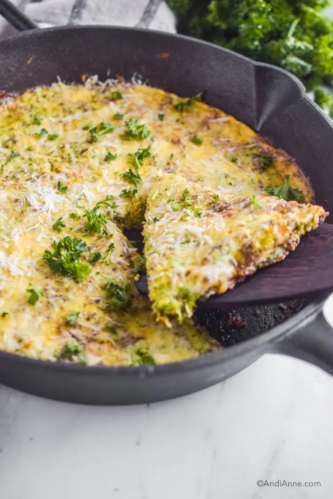 Slice of zucchini parmesan frittata on spatula in black skillet.