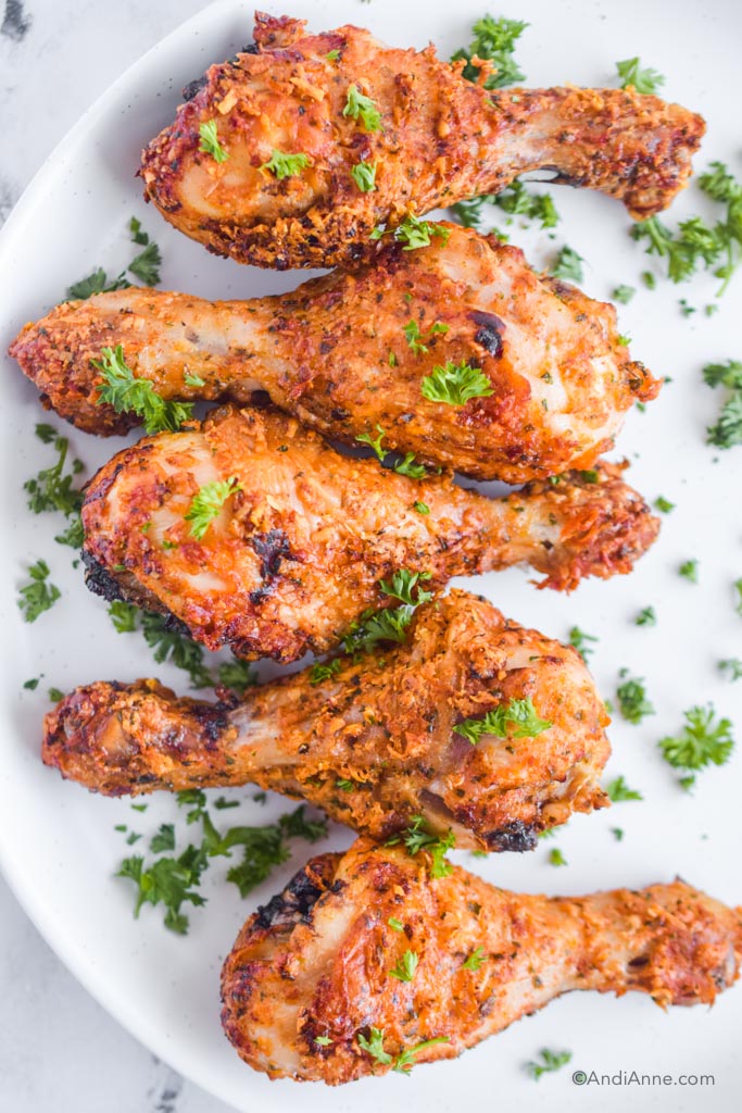 parmesan chicken drumsticks with chopped fresh parsley on white plate