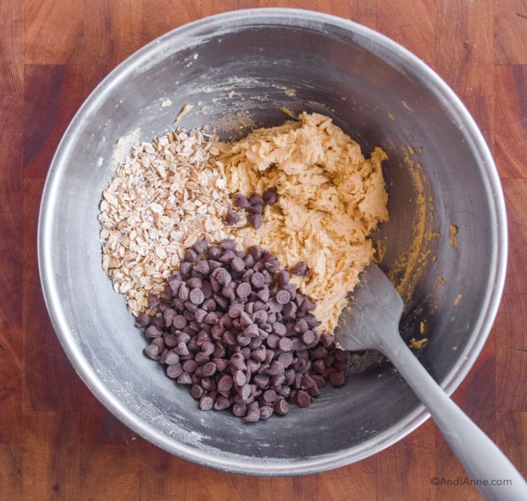 steel bowl with cookie batter, chocolate chips and rolled oats and spatula