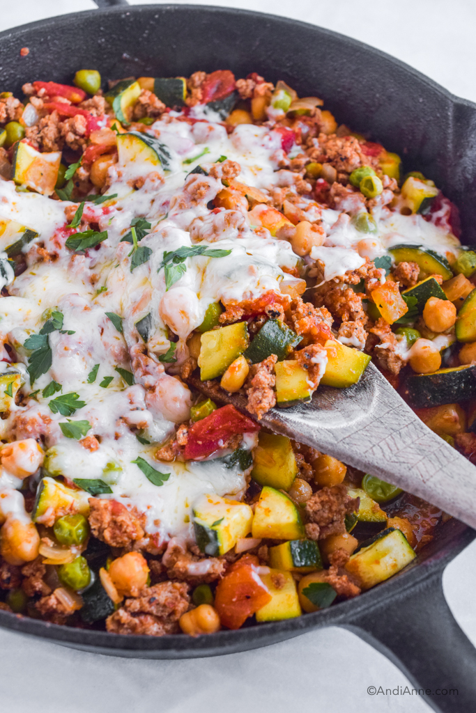 A skillet with chopped zucchini, ground beef, chickpeas and melted mozzarella cheese. 